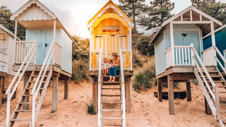 Mother and children sit at the top of the steps at a colourful beach hut